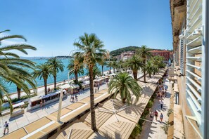 A coastal promenade with palm trees, a clear blue sky, and a view of the sea. - Palms Promenade Luxury Rooms (Split)