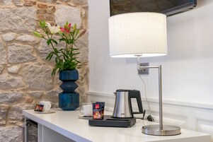 A countertop with a coffee maker, a creamer packet, a cup, and a vase with flowers against a stone wall.