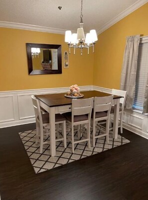 Un coin repas avec une table en bois foncé, des chaises blanches, un lustre et un mur jaune.