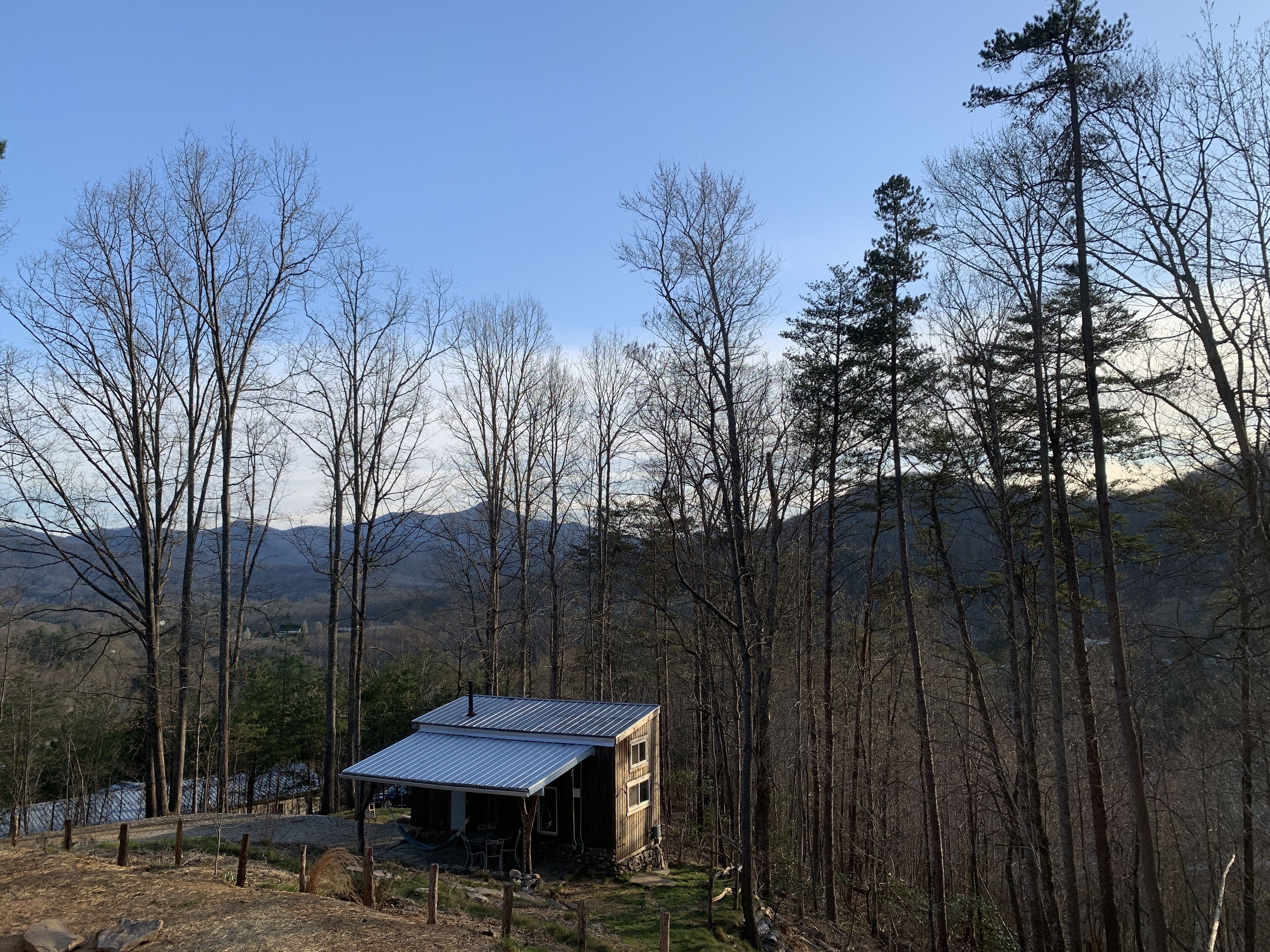 A cabin with a metal roof, surrounded by tall trees and mountains in the background.