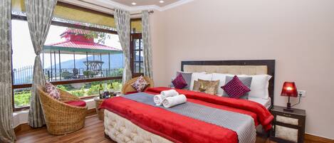 A bedroom with a large bed, a view of a red-roofed building, and a wicker chair.