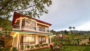 Een tweelaags huis met een balkon, omgeven door groen en een omheind gazon.