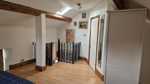 A room with wooden beams, a skylight, a bed, a white wardrobe, and a door leading to another room. - Fully Detached Cottage House Loddington Kettering (Kettering)