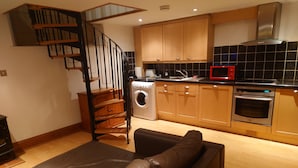 A modern kitchen with wooden cabinets, a built-in oven, and a red microwave. - Fully Detached Cottage House Loddington Kettering (Kettering)