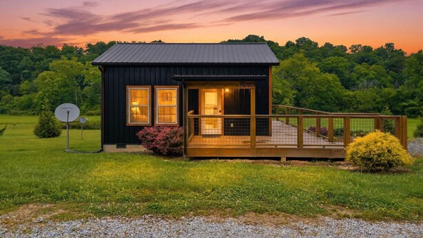 A small, dark-colored cabin with a wooden deck and a satellite dish. - Romantic Smoky Mountain Cabin | Hot Tub | Pet-Friendly (Sevierville)