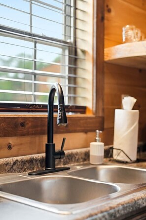 A kitchen sink with a modern faucet, a window with blinds, and a countertop with a soap dispenser. - Romantic Smoky Mountain Cabin | Hot Tub | Pet-Friendly (Sevierville)