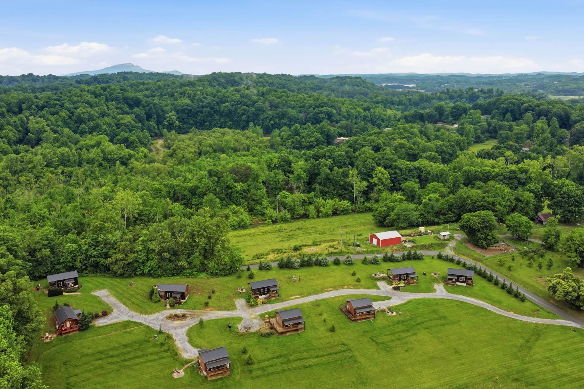 A rural landscape with multiple houses surrounded by green fields and dense forest.