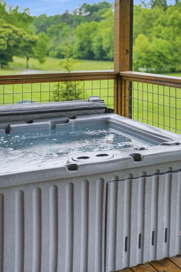 A hot tub on a wooden deck with a view of a green landscape.