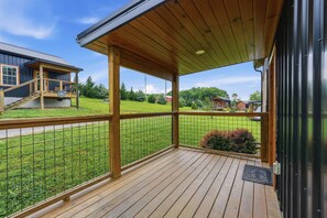 A wooden deck with a metal railing, a covered porch, and a view of a residential area with houses and greenery. - Romantic Smoky Mountain Cabin | Hot Tub | Pet-Friendly (Sevierville)