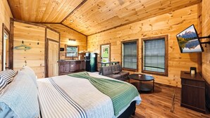 A cozy cabin interior with a bed, a sofa, a dining table, and a kitchen area. - Romantic Smoky Mountain Cabin | Hot Tub | Pet-Friendly (Sevierville)