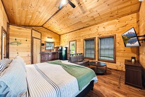A cozy cabin interior with a bed, a sofa, a dining table, and a kitchen area. - Romantic Smoky Mountain Cabin | Hot Tub | Pet-Friendly (Sevierville)