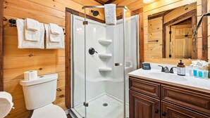 A modern bathroom with a glass-enclosed shower, wooden walls, a white sink, and a large mirror. - Romantic Smoky Mountain Cabin | Hot Tub | Pet-Friendly (Sevierville)