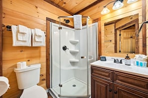 A modern bathroom with a glass-enclosed shower, wooden walls, a white sink, and a large mirror. - Romantic Smoky Mountain Cabin | Hot Tub | Pet-Friendly (Sevierville)