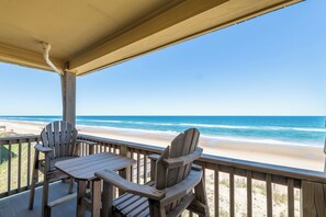 Une terrasse en bois avec deux fauteuils Adirondack et une table, le tout offrant une vue sur la plage.