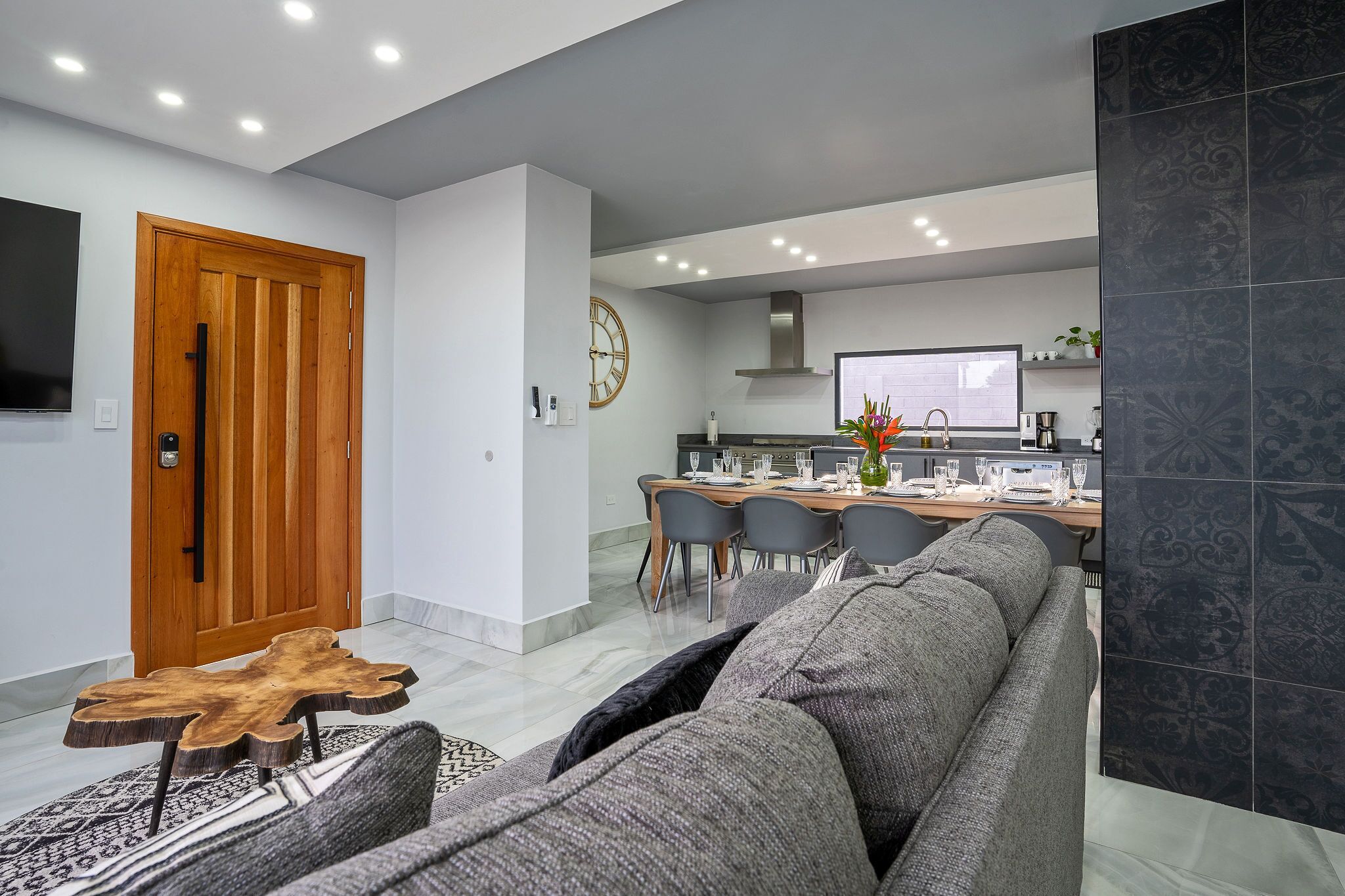 Un salon moderne avec un canapé gris, une table basse en bois et un coin repas avec une table dressée pour quatre personnes.