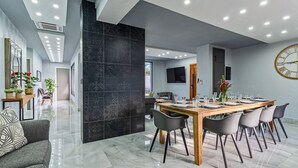 Een moderne eethoek met een lange houten tafel, zwarte stoelen en een grote wandklok.