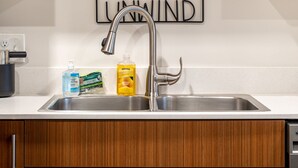 A kitchen with wooden cabinets, a stainless steel sink, and a 'Welcome' sign above the shelves. - Cute Condo | TART Trail | Bikes | AC | Downtown | (Traverse City)