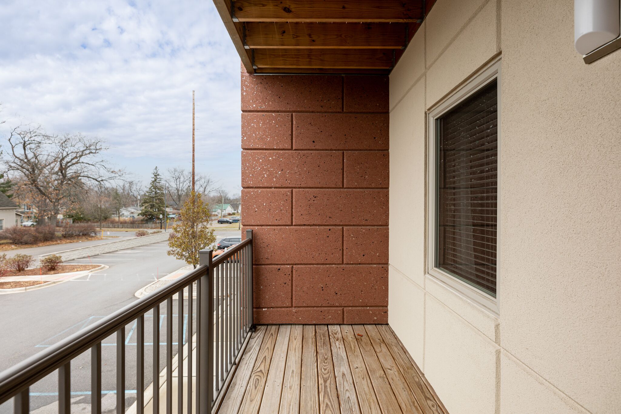 A balcony with a wooden floor and a brick wall, overlooking a street with cars and trees.
