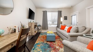 A modern living room with a sofa, ottoman, and a colorful rug. - Cute Condo | TART Trail | Bikes | AC | Downtown | (Traverse City)