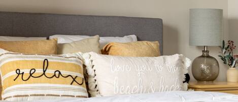 A bedroom with a bed, pillows, a nightstand, a lamp, and a painting of a tree-lined path.