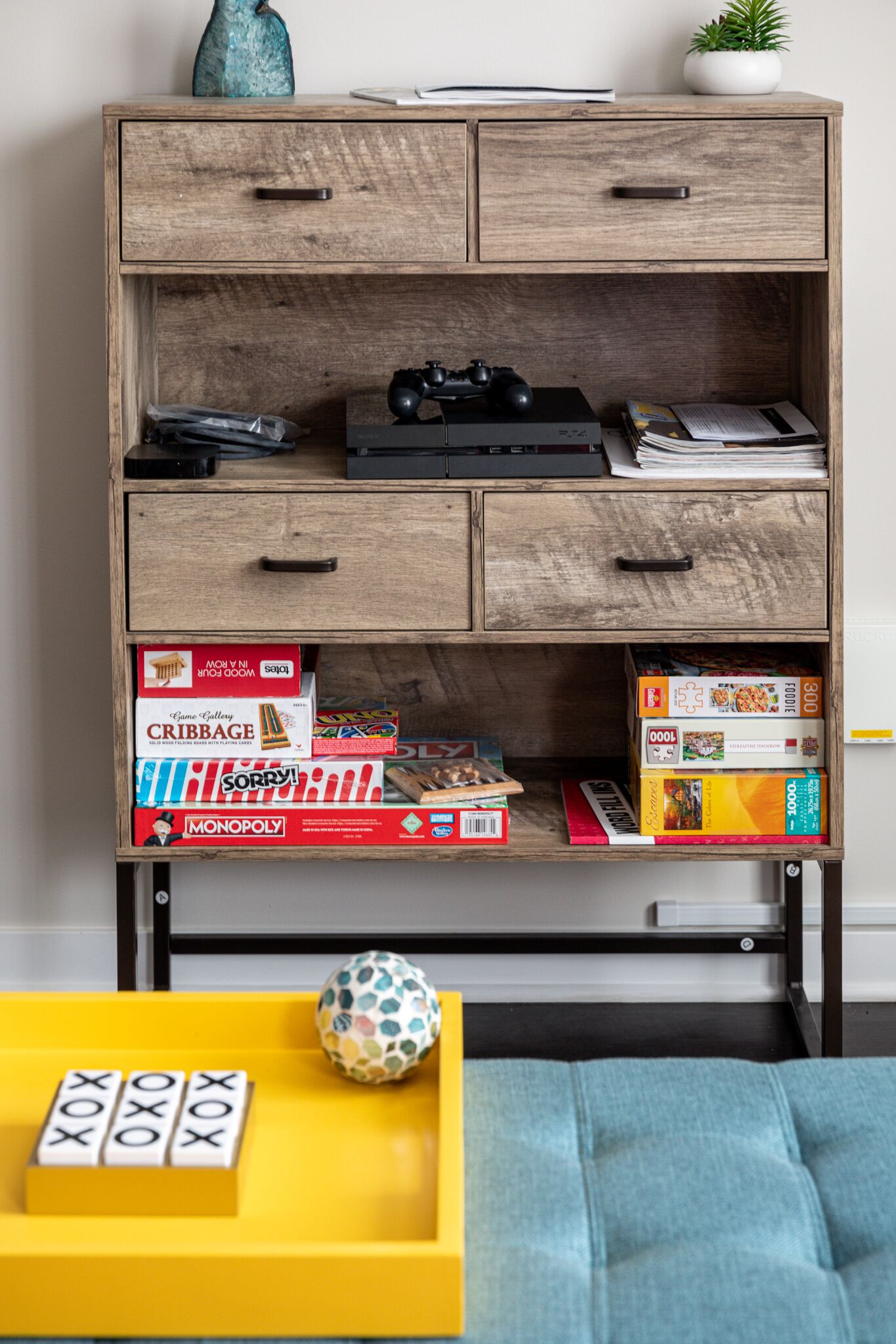 A wooden cabinet with multiple drawers, some containing board games and a video game console.
