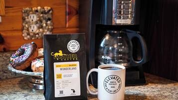A bag of Panther Coffee Wonderland ground coffee, a white mug with a logo, and a coffee maker on a kitchen counter.