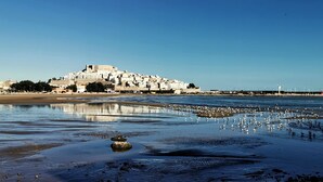 Un pueblo costero con un complejo de edificios blancos destacado, una playa de arena y un litoral rocoso.