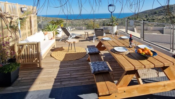 Una terraza con mobiliario de madera, una mesa lista para comer y vista al mar.