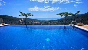 Piscina azul cristalina con dos árboles a cada lado, rodeada por una valla, con vistas a un valle.
