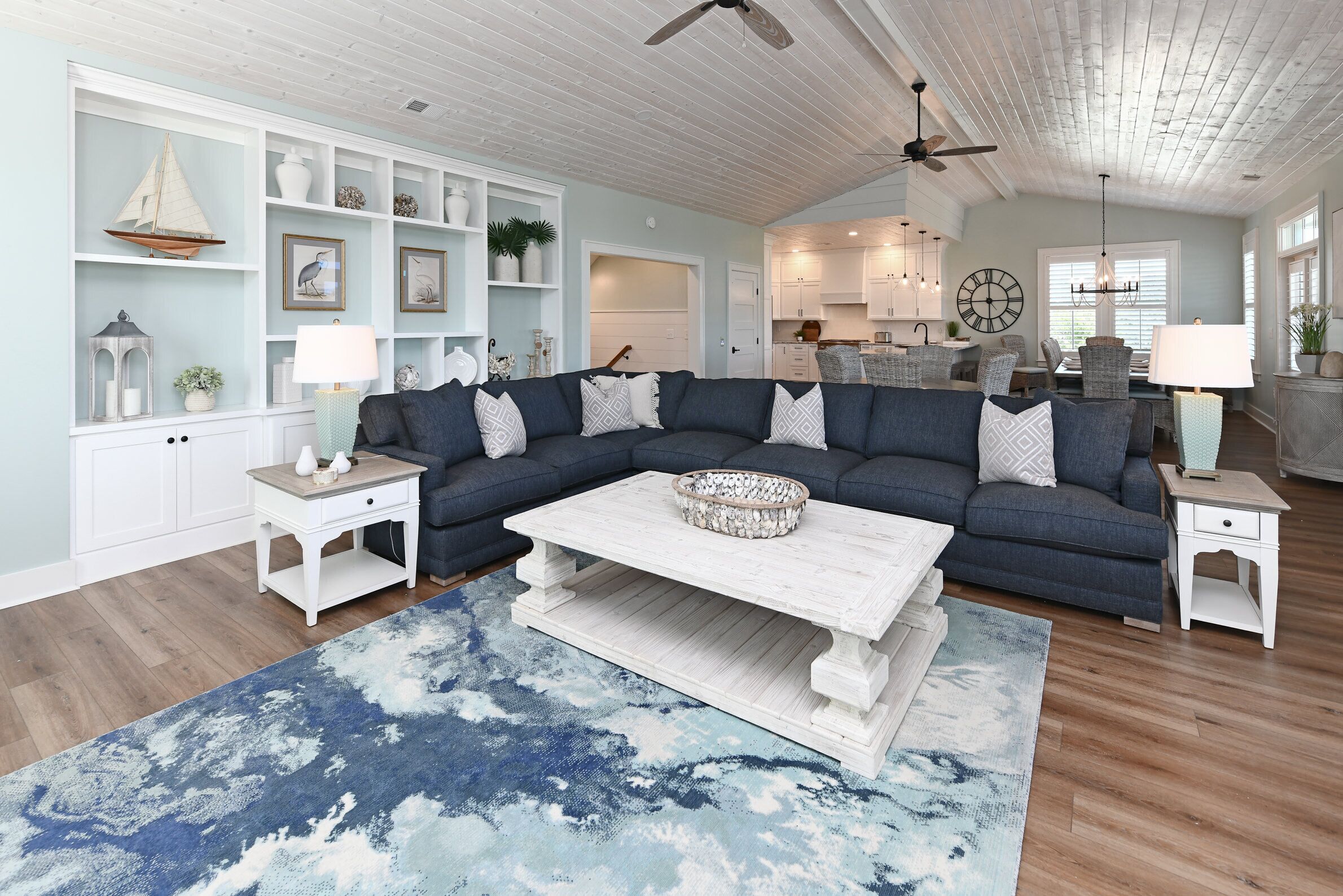 Ein geräumiges Wohnzimmer mit einem dunkelblauen Ecksofa, einem weißen Couchtisch und einem blauen Teppich mit Muster.