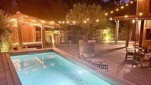 A swimming pool with a wooden deck, surrounded by outdoor furniture and string lights. - Atypical villa "Cabane Oléron" with heated swimming pool (Saint-Trojan-les-Bains)