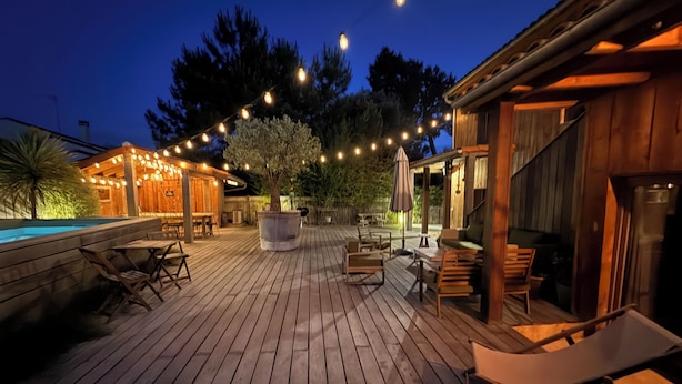 A wooden deck with outdoor seating, a pool, and string lights. - Atypical villa "Cabane Oléron" with heated swimming pool (Saint-Trojan-les-Bains)
