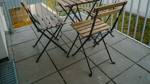 Un pati amb una taula i cadires de fusta, una planta en test i una barana de metall.