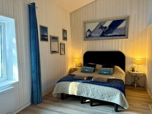 A room with a bed, two bedside tables, a window with curtains, and a wall with framed pictures. - Townhouse "La Petite Rochelaise" (La Jarne)