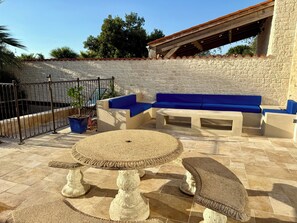 A patio with stone flooring, a blue cushioned seating area, and a round table with stone legs. - Townhouse "La Petite Rochelaise" (La Jarne)