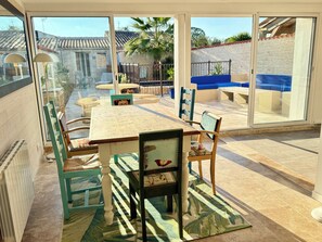 Un comedor con mesa y sillas, ventanas amplias y vistas a una piscina y jardín.