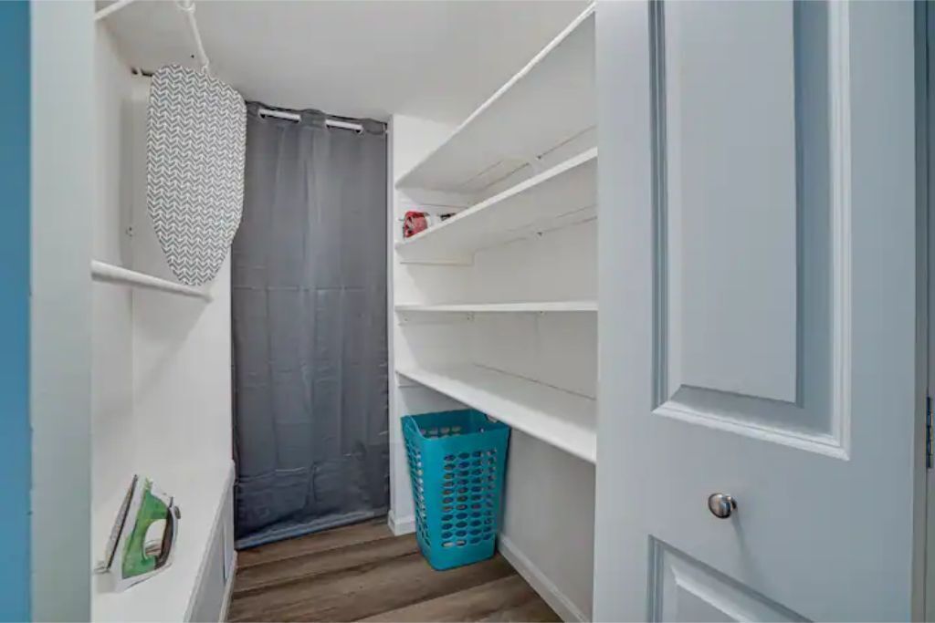 A narrow hallway with white shelves, a grey curtain, and a blue laundry basket.
