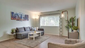 A modern living room with a grey sofa, a white coffee table, and a grey armchair. There is a cityscape painting on the wall and a floor lamp.
