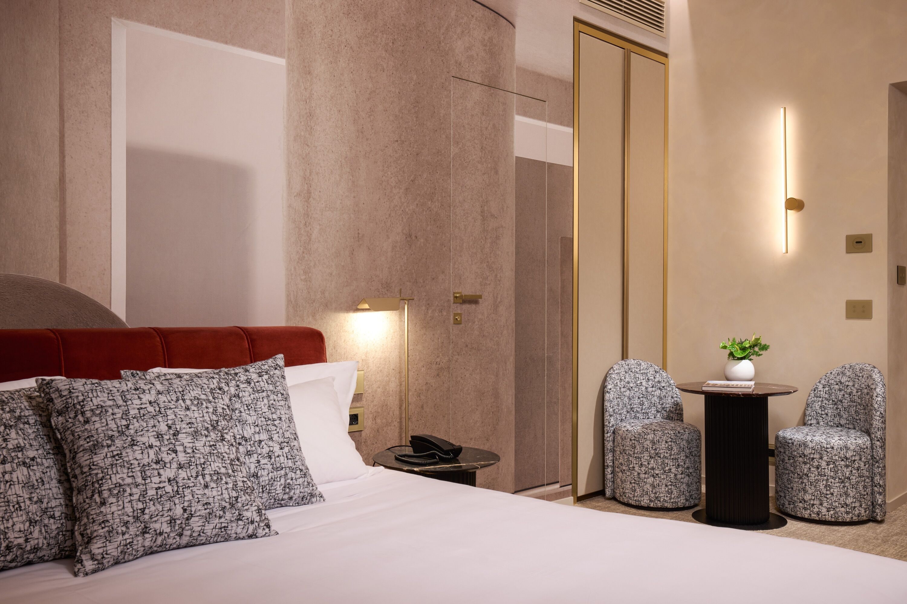 Une chambre d’hôtel avec un grand lit, deux fauteuils rembourrés, une petite table avec un vase et un téléphone sur une table de chevet.