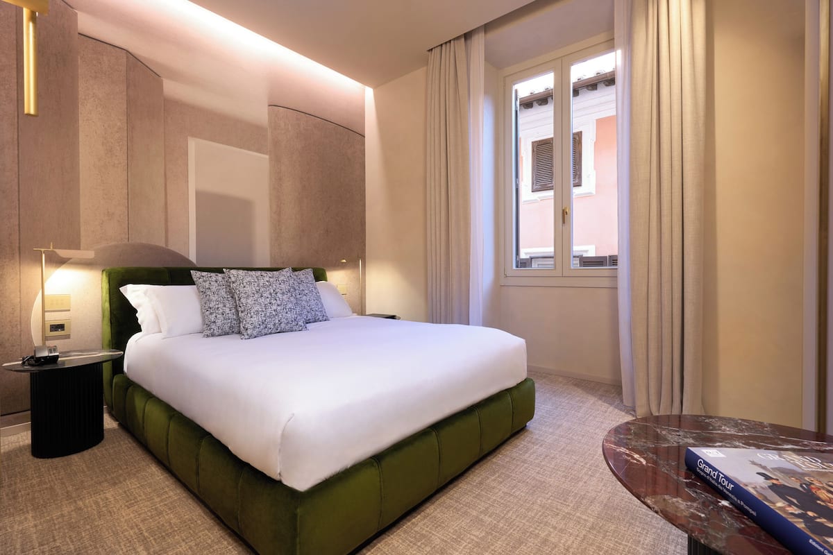 A hotel room with a large bed, a nightstand, a reading table, and a window with curtains.