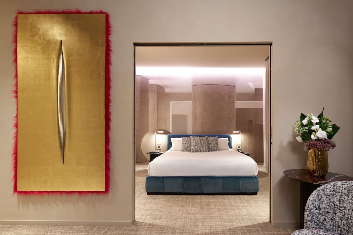 A modern hotel room with a large bed, a decorative wall piece, and a vase with flowers.