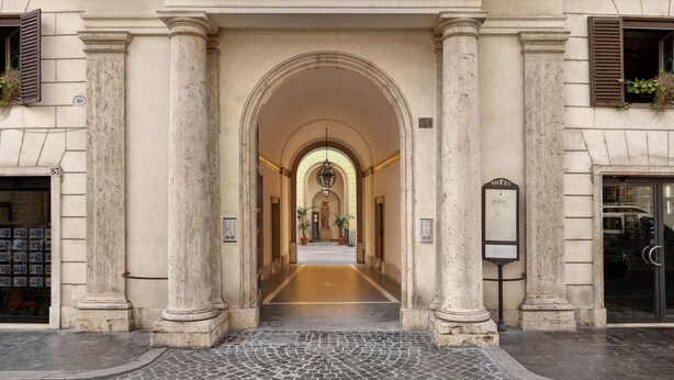 A grand entrance with a central archway flanked by columns, leading to a spacious corridor with a tiled floor. - Borghese Contemporary Hotel (Rome)