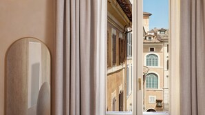 A view through a window with curtains, revealing a building with multiple windows and shutters. - Borghese Contemporary Hotel (Rome)