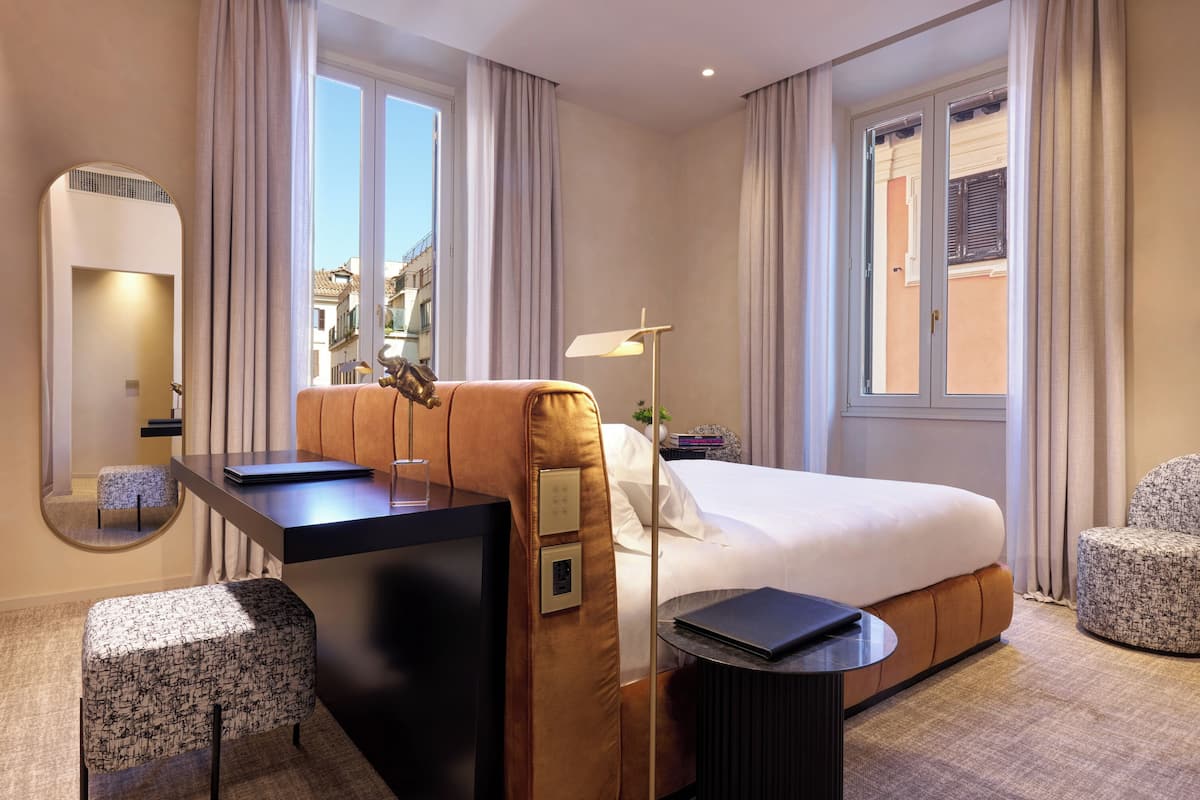 A hotel room with a bed, a desk, a chair, a mirror, and a window with curtains.