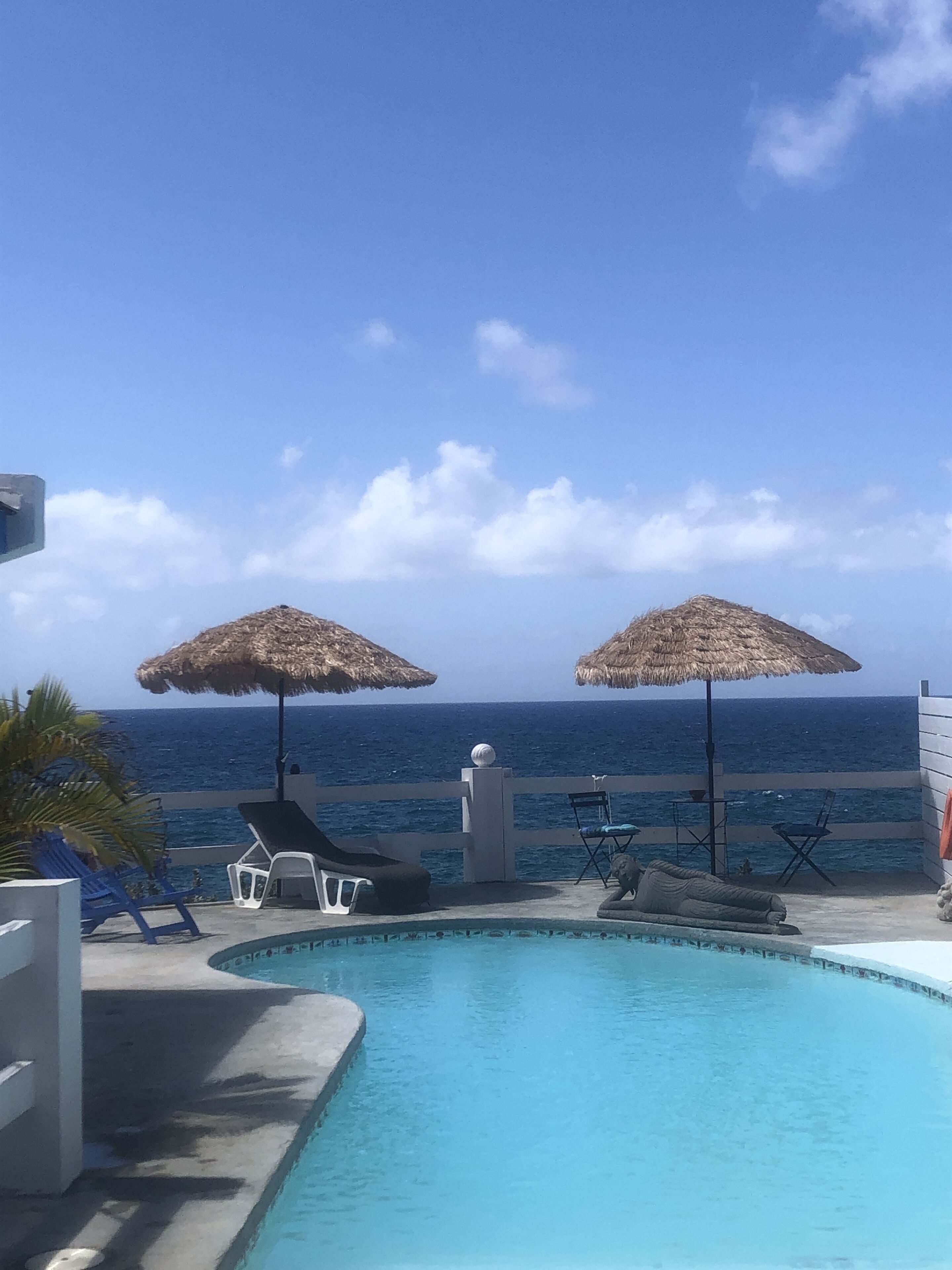 A pool area with two thatched umbrellas, lounge chairs, and a view of the ocean.