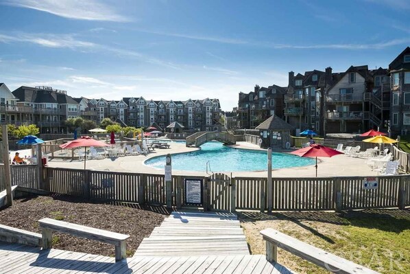 A pool area with a wooden deck, lounge chairs, and umbrellas.