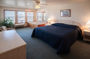Un dormitorio con una cama grande, un escritorio, una silla, una mesita, un rincón con asiento junto a la ventana y un ventilador de techo.