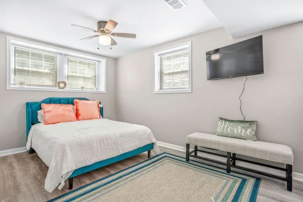 A bedroom with a bed, a bench, a ceiling fan, and a TV.
