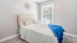 Un dormitorio con cama, ventilador de techo, ventana con persianas y un adorno en la pared.