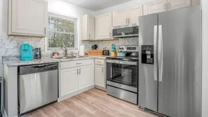 Una cocina moderna con electrodomésticos de acero inoxidable, armarios blancos y encimera de mármol.